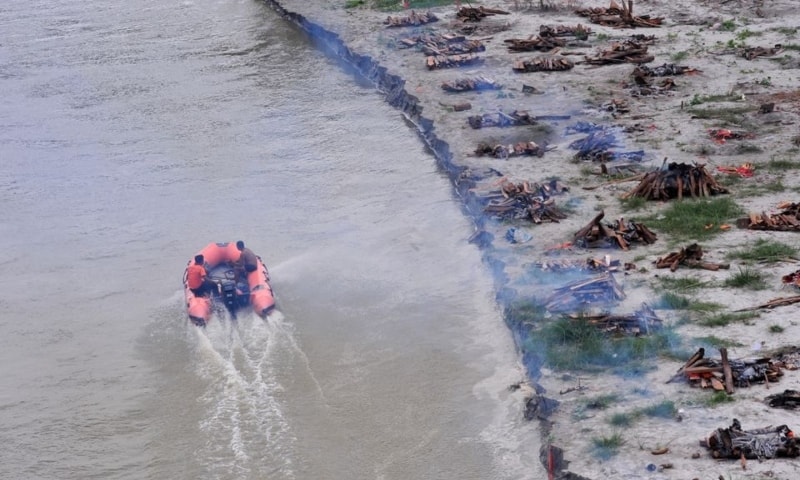 Members of State Disaster Response Force patrol in the Ganges river past burning pyres of bodies that washed up on its banks after monsoon rains swelled it and exposed shallow sand graves dug during the peak of the latest Covid-19 wave in Phaphamau, Prayagraj, India, June 25. — Reuters Members of State Disaster Response Force patrol in the Ganges river past burning pyres of bodies that washed up on its banks after monsoon rains swelled it and exposed shallow sand graves dug during the peak of the latest Covid-19 wave in Phaphamau, Prayagraj, India, June 25. — Reuters