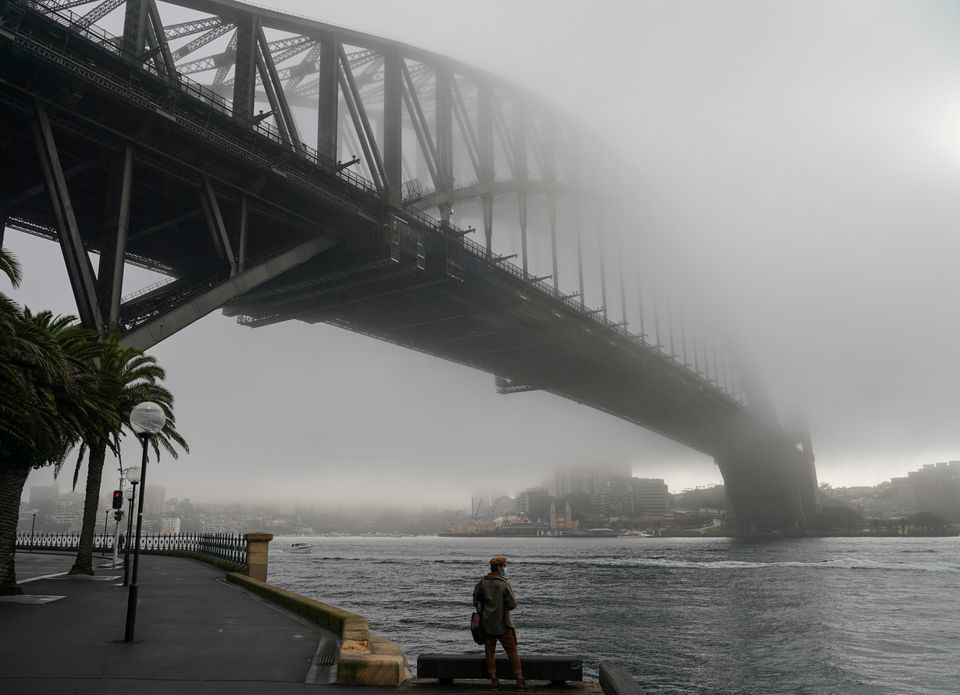 A man wearing a protective face mask takes in the waterfront view underneath the Sydney Harbour Bridge, seen shrouded in fog, during a lockdown to curb the spread of a coronavirus outbreak in Sydney, Australia, June 30. — Reuters