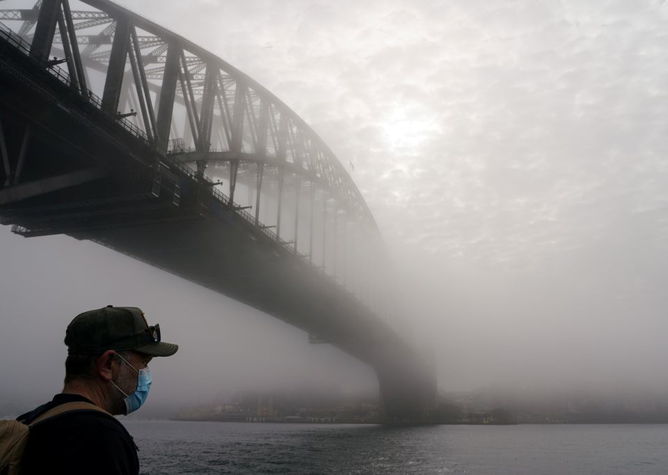 A man wearing a protective face mask takes in the waterfront view under the Sydney Harbour Bridge, seen shrouded in morning fog, during a lockdown to curb the spread of a coronavirus outbreak in Sydney, Australia, July 1. — Reuters