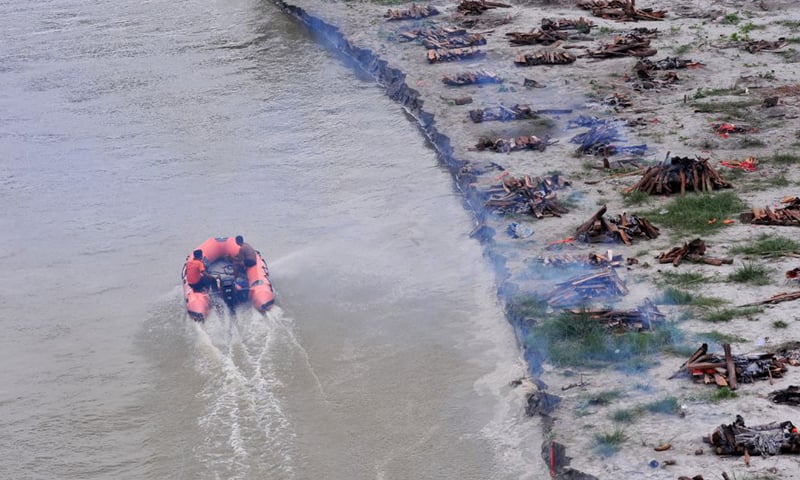 Members of the State Disaster Response Force patrol in the Ganges River past burning pyres of bodies that washed up on its banks after monsoon rains swelled it and exposed shallow sand graves dug during the peak of the latest Covid19 wave in Phaphamau, India. &mdash; Reuters/File