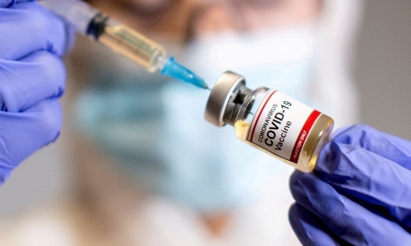 A woman holds a small bottle labeled with a "Covid-19 vaccine" sticker and a medical syringe in this illustration taken October 30. — Reuters/File