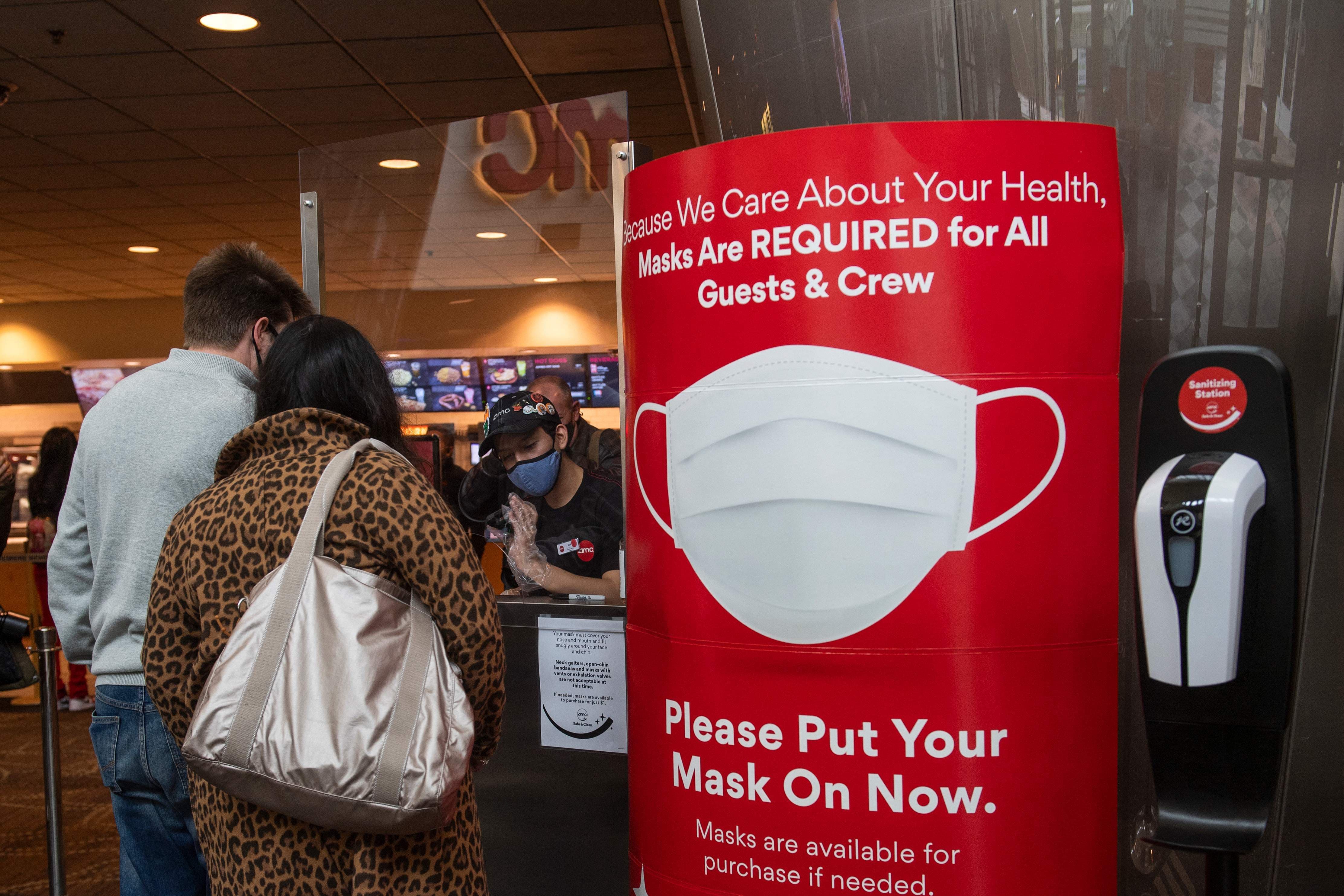 In this file photo taken on March 15, a sign asking people to wear a mask is displayed as moviegoers buy tickets at the AMC Burbank theatre on reopening day in California. — AFP