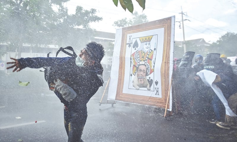 BANGKOK: A pro-democracy protester throws an object at police as others take cover from water cannon behind a derogatory image of Thailand’s prime minister during a march on the Government House on Sunday.—AFP