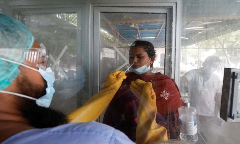 A paramedic wearing protective gear takes a nasal swab of a woman at a glass booth, to be tested for Covid-19. — Reuters/File