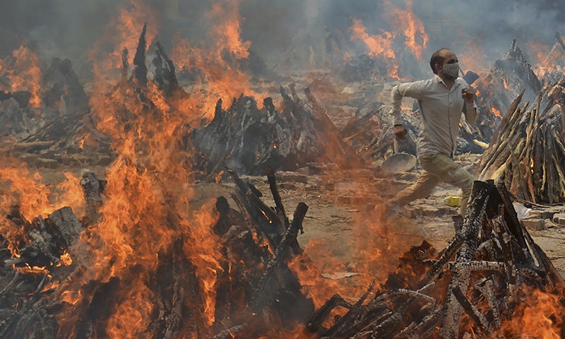 In this April 29 file photo, a man runs to escape heat emitting from the multiple funeral pyres of Covid-19 victims at a crematorium in the outskirts of New Delhi, India. &mdash; AP