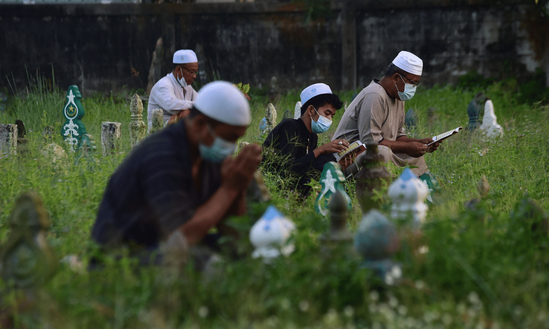 People pray next to the grave of relatives at a cemetery during Eidul Azha in Thailand's southern province of Narathiwat. — AFP