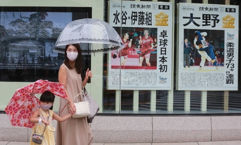 People wearing face masks to protect against the spread of the coronavirus walk past extra papers reporting on Japanese gold medalists at Tokyo Olympics, in Tokyo on July 27. — AP