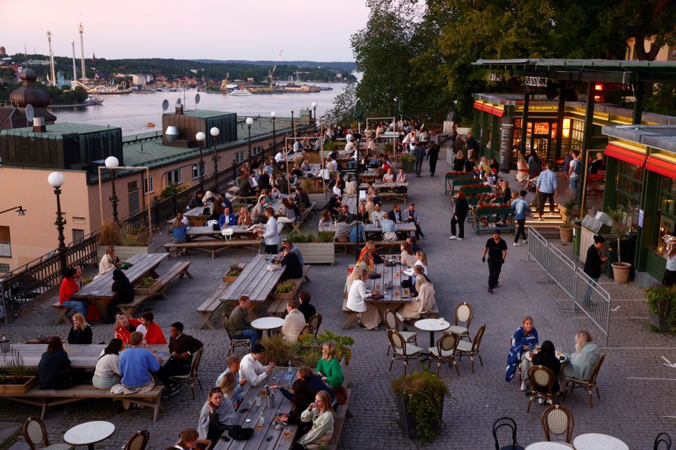 People sit at tables at an outdoor bar in Stockholm, Sweden, July 1. &mdash; Reuters