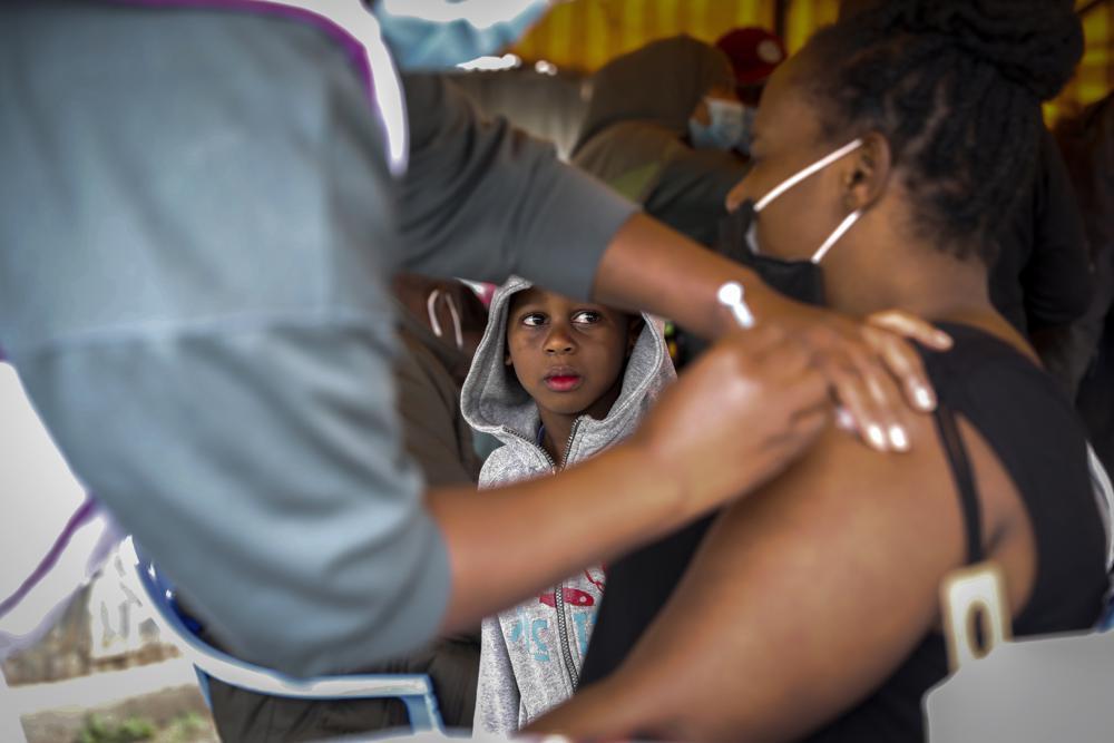 A Kenyan woman receives a dose of AstraZeneca coronavirus vaccine donated by Britain, as her son watches, at the Makongeni Estate in Nairobi, Kenya on Aug 14. &mdash; AP