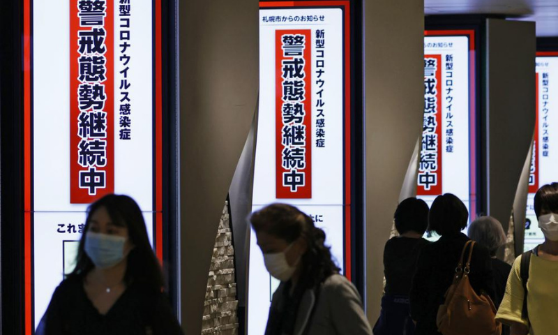 People wearing face masks walk by signs that read, "Under the coronavirus state of emergency," in Sapporo, Hokkaido region, northern Japan, on Wednesday. &mdash; AP