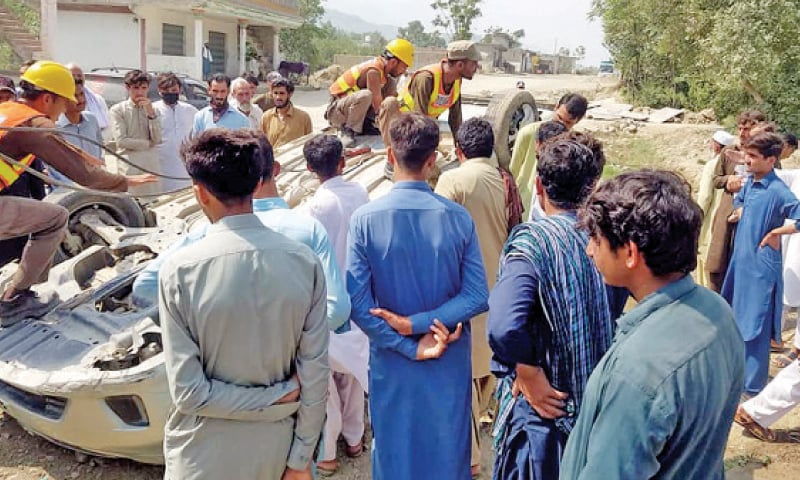 Rescuers and people surround a car that overturned in Gardai area of Utmankhel tehsil on Saturday. &mdash; Dawn