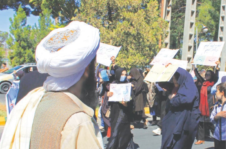 Herat: A member of the Taliban watches as Afghan women hold placards during a protest on Thursday.—AFP