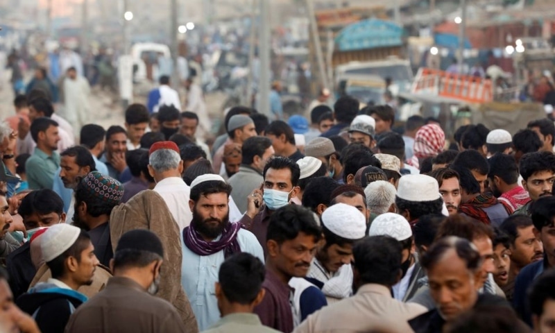 A man wearing a protective mask walks through a crowd of people along a makeshift market in Karachi on January 17. — Reuters