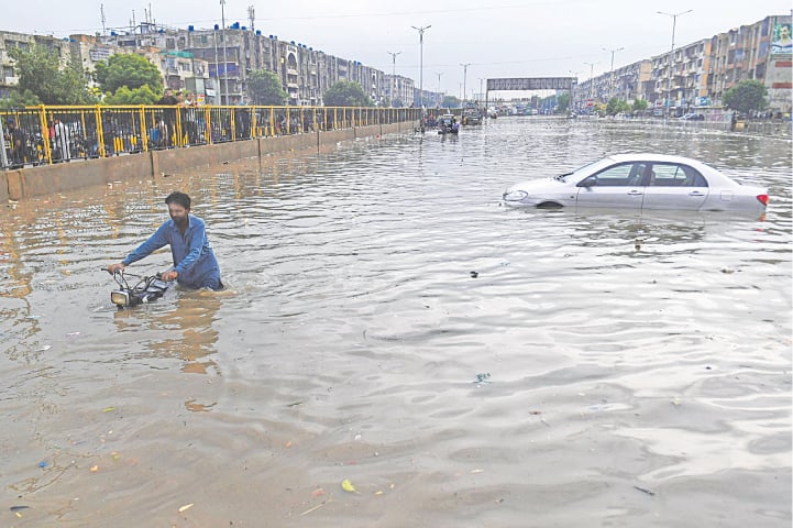 KARACHI: A man pushes his motorbike through a flooded street while a car floats behind after heavy rain on Thursday. As the city received downpour, the authorities warned that the situation was unlikely to improve because the kilometres-long infrastructure of the yet-to-start Green Line bus service had badly affected the Central district’s drainage and sewerage system.—AFP