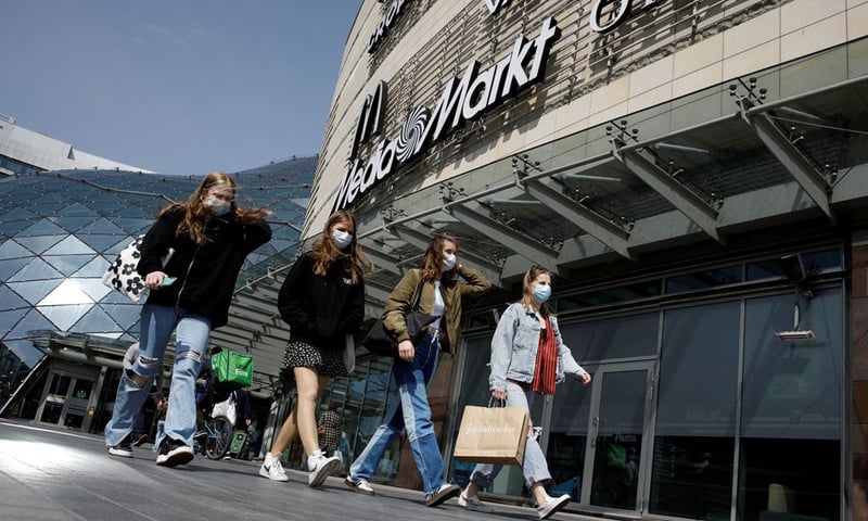 In this file photo, people wearing masks walk in front of the Zlote Tarasy shopping mall in Warsaw, Poland. &mdash; Reuters/File