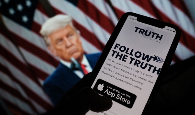 This illustration photo shows a person checking the app store on a smartphone for “Truth Social”, with a photo of former US president Donald Trump on a computer screen in the background, in Los Angeles, on Wednesday. — AFP