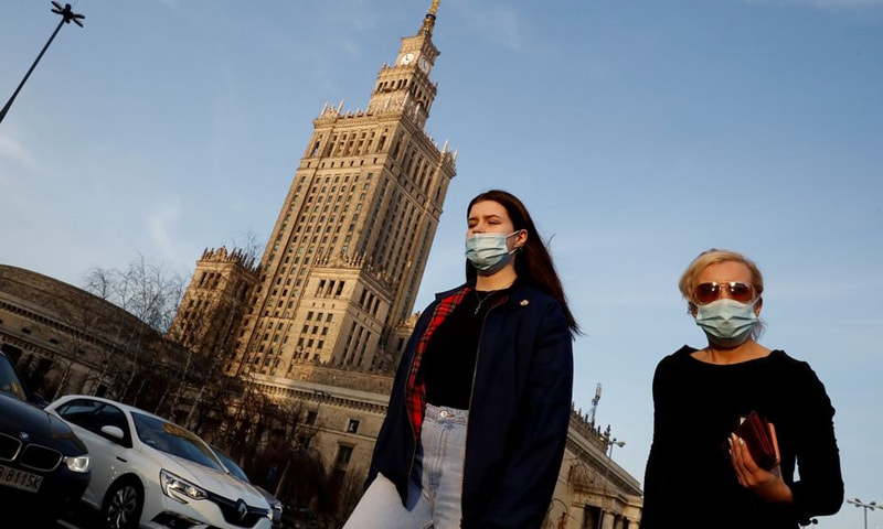 In this file photo, people wearing protective masks walk in front of the Palace of Culture and Science in Warsaw, Poland. — Reuters/File