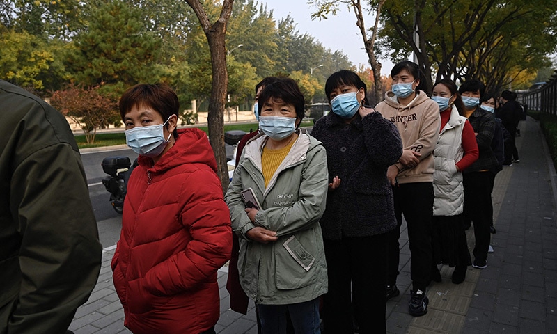 People wait in line to receive Covid-19 vaccination booster shots along a street in Beijing on Saturday. — AFP
