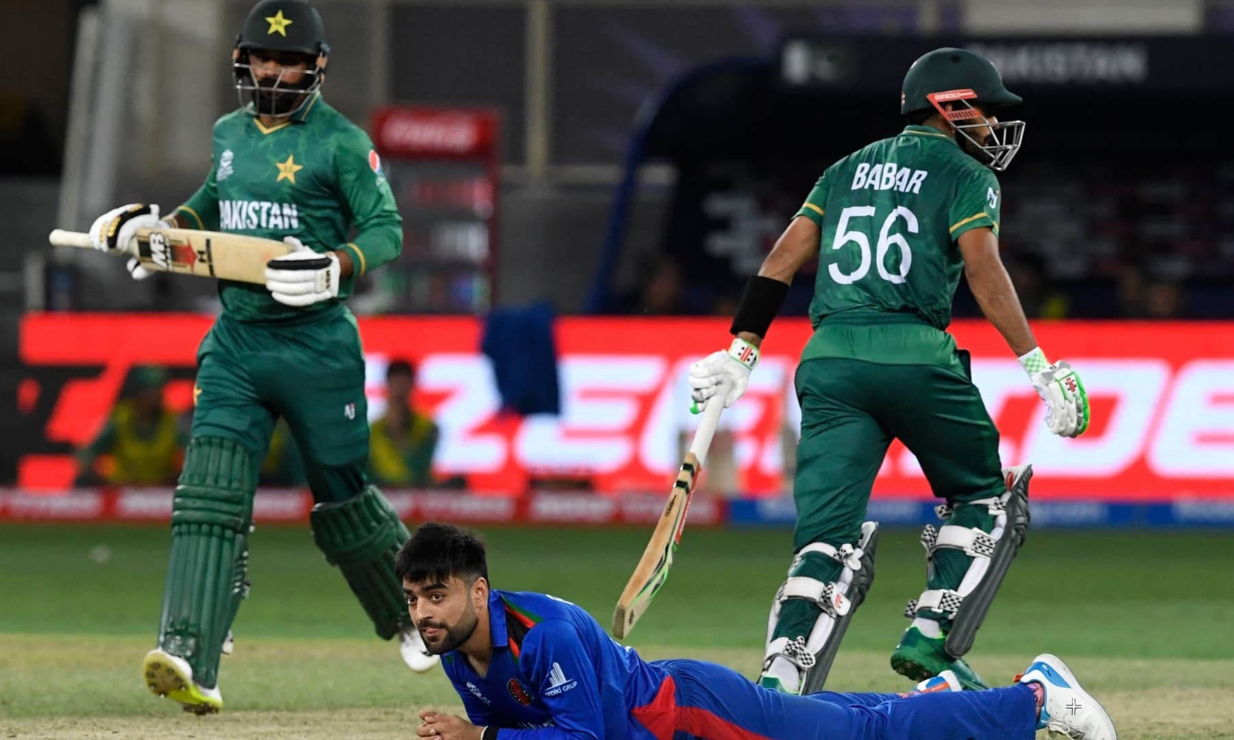 Afghanistan's Rashid Khan falls on the ground as captain Babar Azam (R) and Mohammad Hafeez run between the wickets during the ICC men’s Twenty20 World Cup cricket match between Afghanistan and Pakistan at the Dubai International Cricket Stadium in Dubai on October 29, 2021. — AFP