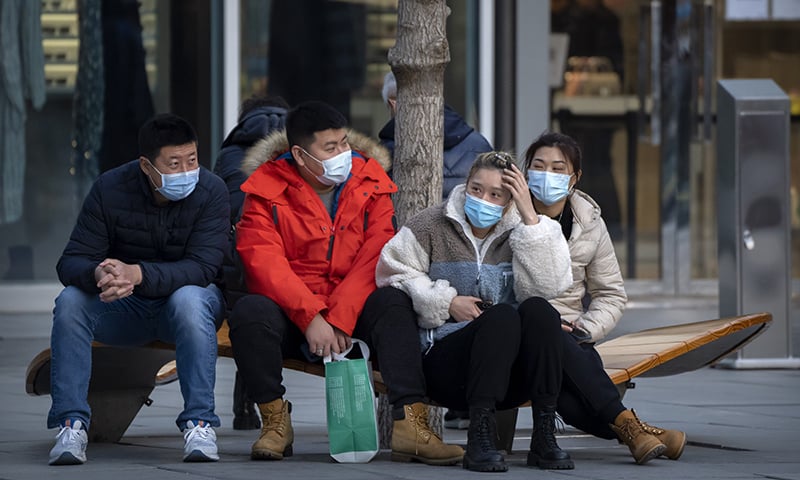 People wearing face masks to protect against Covid-19 sit on a bench at an outdoor shopping centre in Beijing on November 13. &mdash; AP
