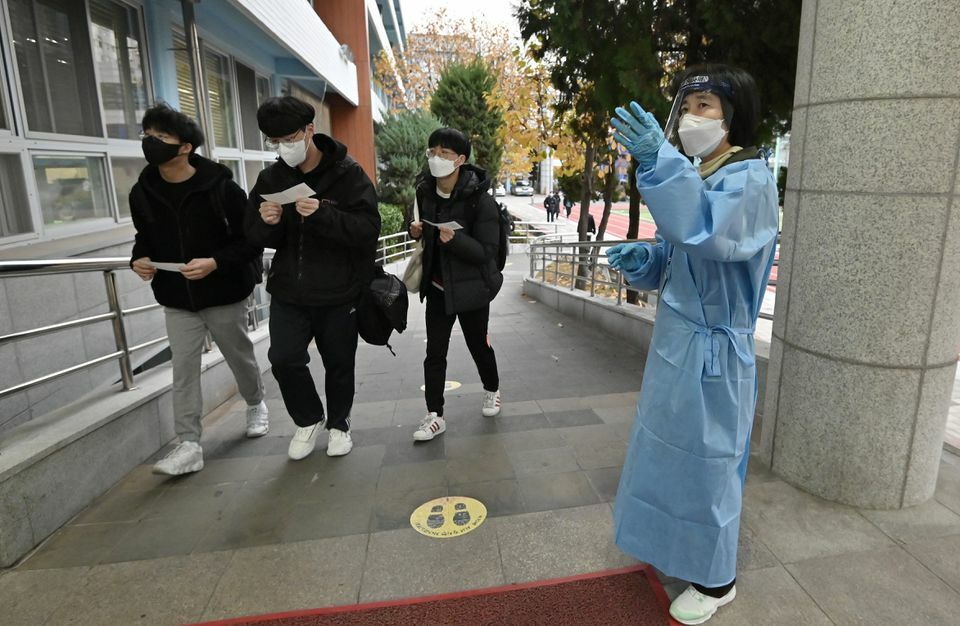 A school teacher wearing personal protective equipment guides students arriving for a nationwide university entrance exam amid a coronavirus outbreak at a school in Seoul, South Korea, November 18. — Reuters