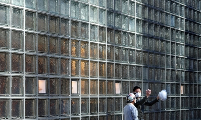 Workers wearing protective masks to help curb the spread of the coronavirus speak near a glass wall of a building in Tokyo. — AP