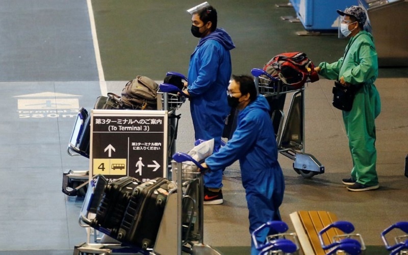 Men wearing protective suits make their way at a bus stop at Narita international airport on the first day of closed borders on Nov 30, 2021. &mdash; Reuters