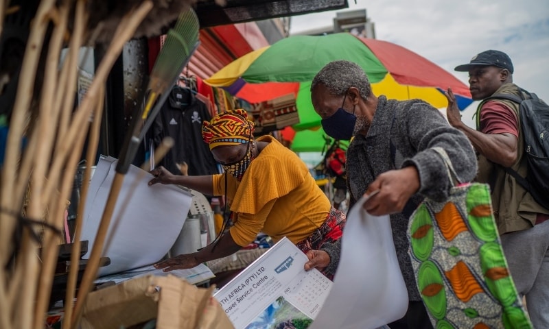 A masked couple sorts through goods at an outdoor market near the Baragwanath taxi rank in Soweto, South Africa, on Dec 2. — AP