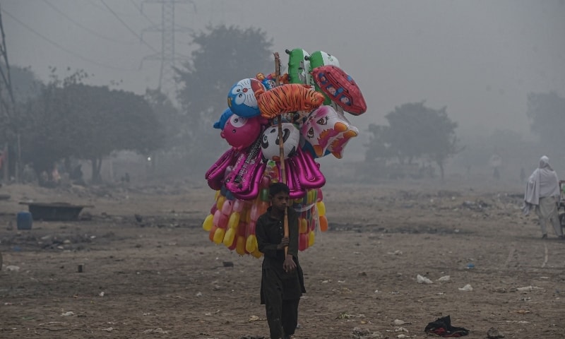 A young street vendor carries balloons as he waits for customers amid smoggy conditions in Lahore on December 2. — AFP