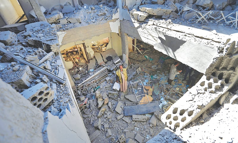 SANAA: Workers walk through the debris of a building destroyed following a reported air strike by the Saudi-led coalition on the Houthi-held Yemeni capital’s international airport on Tuesday.—AFP