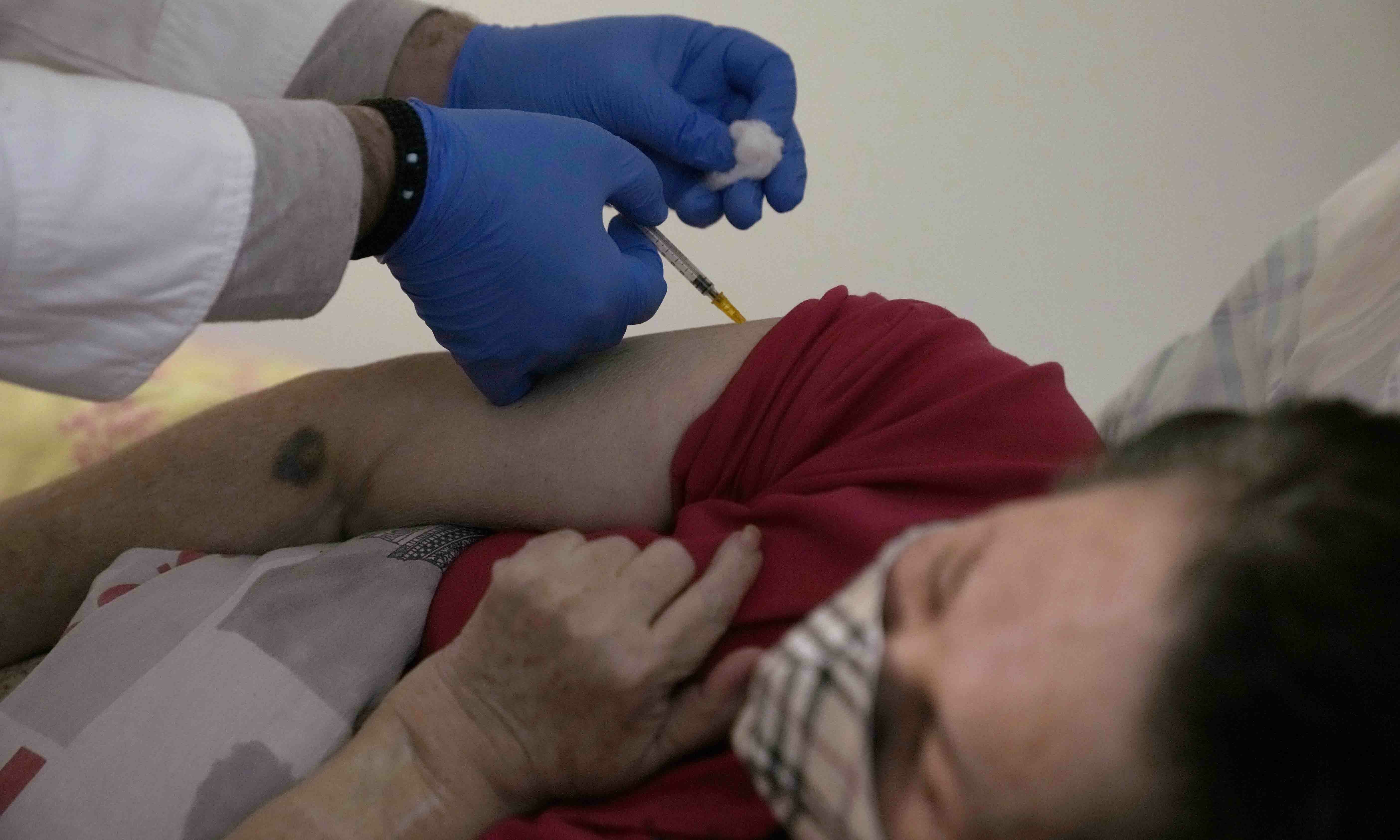 Nurse Panagiotis Bozionelos administers a booster Pfizer-BioNTech vaccine against Covid-19 to Eleni Louka, 74, at her home in Athens on Dec 22. &mdash; AP