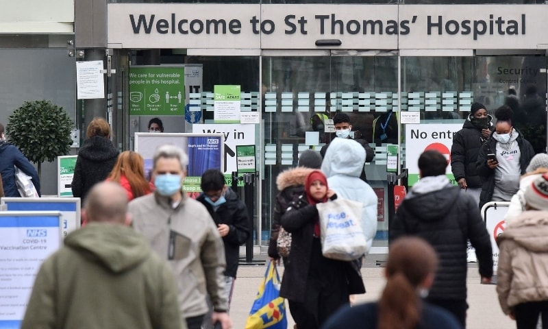 People, some wearing face coverings to combat the spread of Covid-19, arrive at and depart from St Thomas' hospital in central London on December 23. — AFP