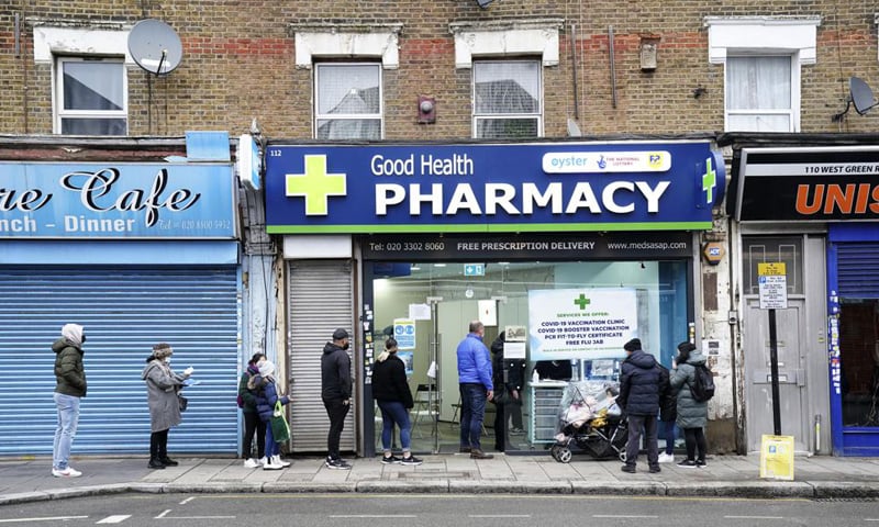 People wait in line to receive a 'Jingle Jab' booster injection at the Good Health Pharmacy in north London. — AP