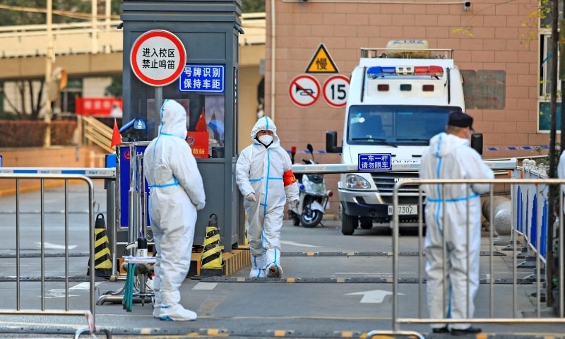 Workers in protective suits stand at an entrance to a university's residential area under lockdown following the Covid-19 outbreak in Xian, Shaanxi province, China on December 20. — Reuters