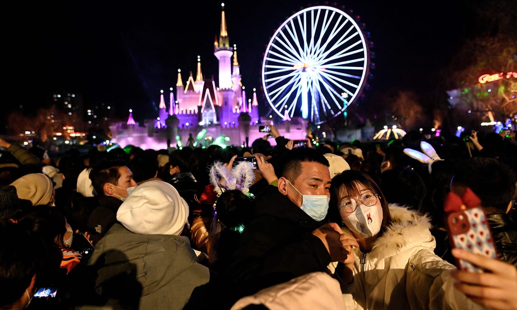 People wearing face masks attend a New Year's countdown at an amusement park in Beijing on December 31. — AFP