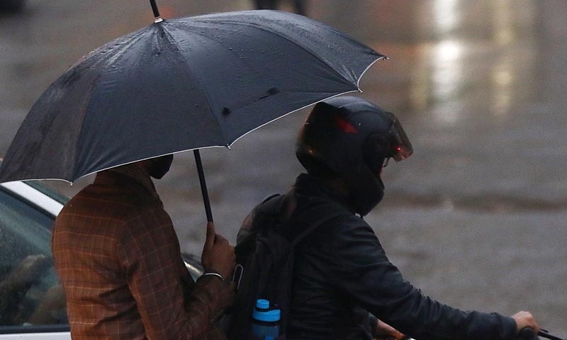 A commuter on a motorcycle holds an umbrella during rain in Karachi. — INP