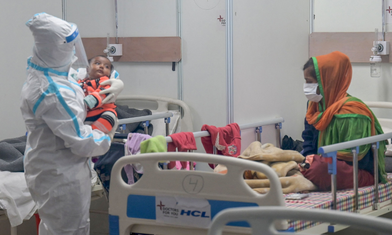 A health worker wearing a personal protective equipment (PPE) suit comforts a Covid-19-infected child as the mother looks on inside a ward at the Commonwealth Games (CWG) village sports complex, temporarily converted into coronavirus care centre, in New Delhi, on Wednesday. &mdash; AFP