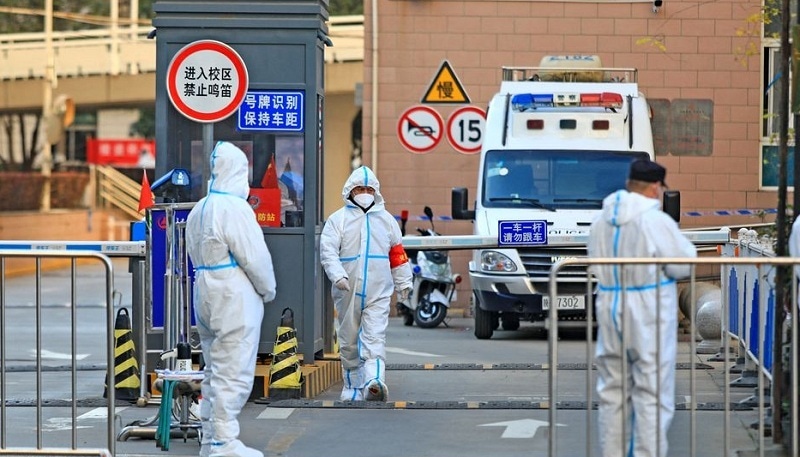 Workers in protective suits stand at an entrance to a university's residential area under lockdown following the coronavirus disease outbreak in Xian, Shaanxi province, China on Dec 20, 2021. &mdash; Reuters