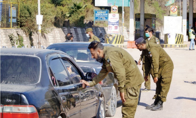 Police personnel check identity cards of people on board vehicles near the Satra Meel toll plaza on Friday as only residents of Murree and Galiyat are permitted to proceed further. — Online