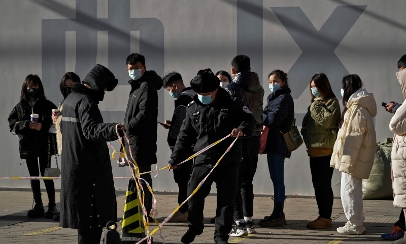 Security guards set up the barricade line as people line up to get a nasal swab for the Covid-19 test to meet traveling requirements at a mobile coronavirus testing facility outside a commercial office buildings in Beijing on January 16. &mdash; AP