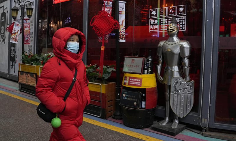 A woman wearing a mask to protect from the coronavirus walks past a coat of armour displayed outside a restaurant in Beijing, China. ─ AP