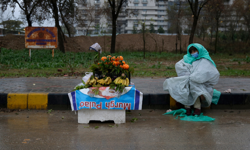 A street vendor covers herself with a plastic sheet to protect from the rain as she waits for customers in Islamabad on Sunday. — AP A street vendor covers herself with a plastic sheet to protect from the rain as she waits for customers in Islamabad on Sunday. — AP
