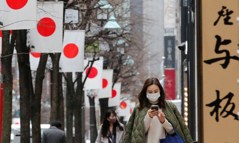 In this file photo, a pedestrian, wearing a protective mask, walks underneath Japanese national flags at a shopping district in Tokyo, Japan. — Reuters/File