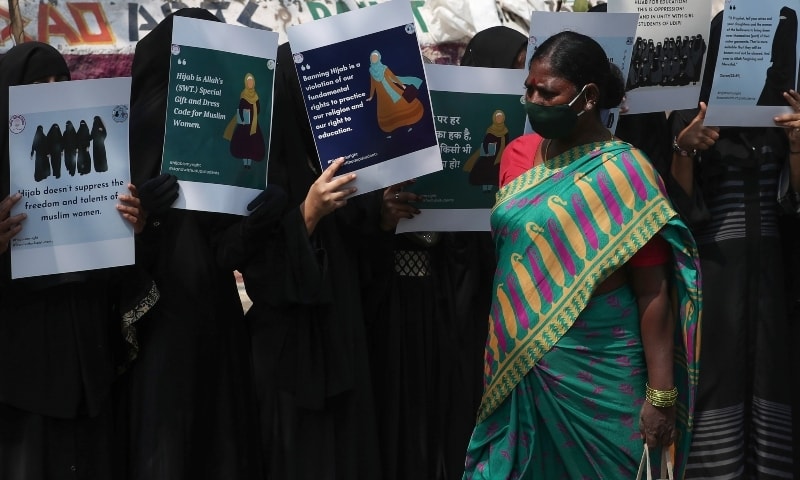 A Hindu woman walks as Muslim women holds placards during a protest against banning Muslim girls wearing hijab from attending classes at some schools in the southern Indian state of Karnataka, in Hyderabad, India, Feb 15. &mdash; AP