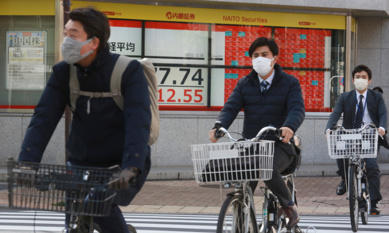 People cycle past an electronic stock board of a securities firm in Tokyo on Wednesday. &mdash; AP
