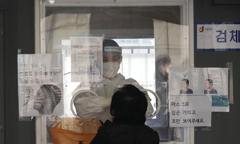 A medical worker in a booth takes a nasal swab sample from a woman at a makeshift testing site in Seoul, South Korea on Tuesday. — AP