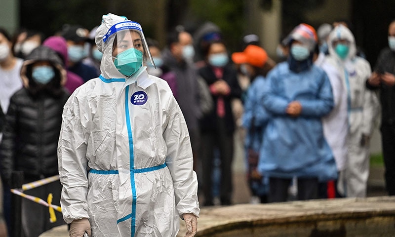 A worker wearing protective gear looks on as people wait to be tested for the coronavirus at a residential compound in Shanghai on Wednesday. &mdash; AFP