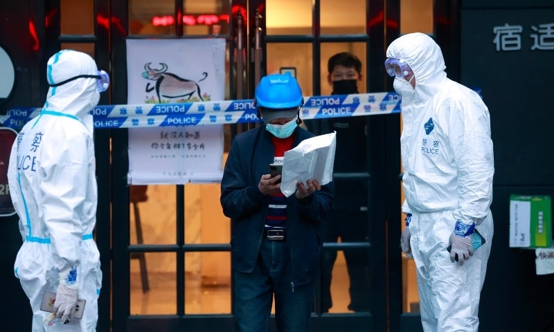 A delivery man walks by police officers with protective suit outside of a hotel in Shanghai, China, on March 15. — AP