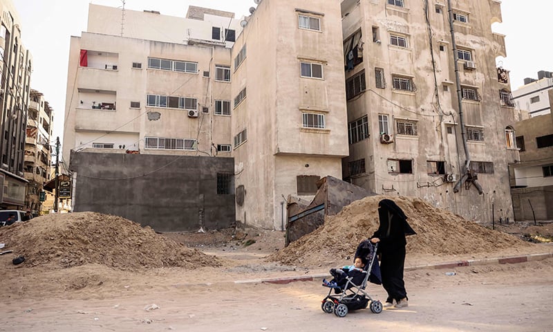 A Palestinian woman pushes a baby stroller past the site where the Abu al-Ouf building stood on Wehda street, on April 26, 2022. —Mahmud Hams/AFP A Palestinian woman pushes a baby stroller past the site where the Abu al-Ouf building stood on Wehda street, on April 26, 2022. —Mahmud Hams/AFP