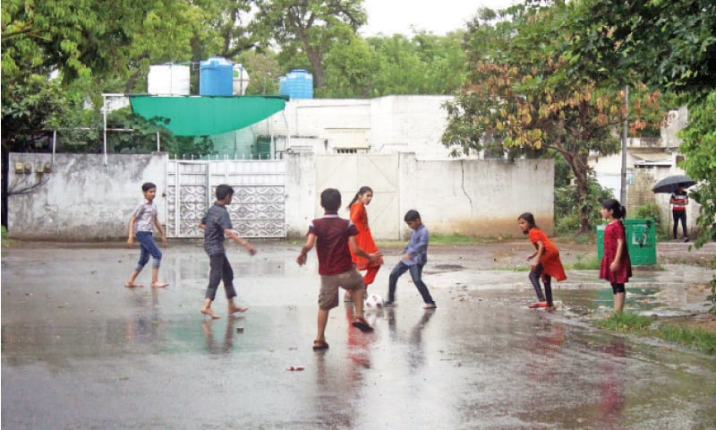 Children play football in a street of G-7 in Islamabad during rain on Thursday. — Online